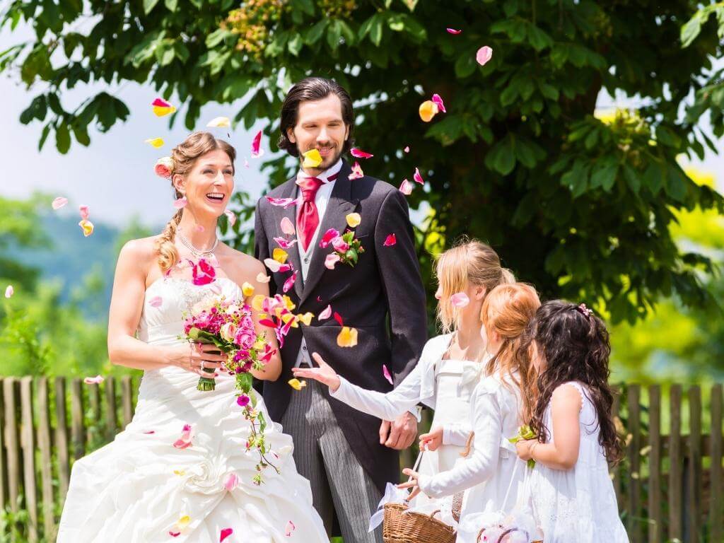 Hochzeitsbilder Ideen mit Kindern: Braut und Bräutigam werden von drei Kindern mit Blütenblättern beworfen