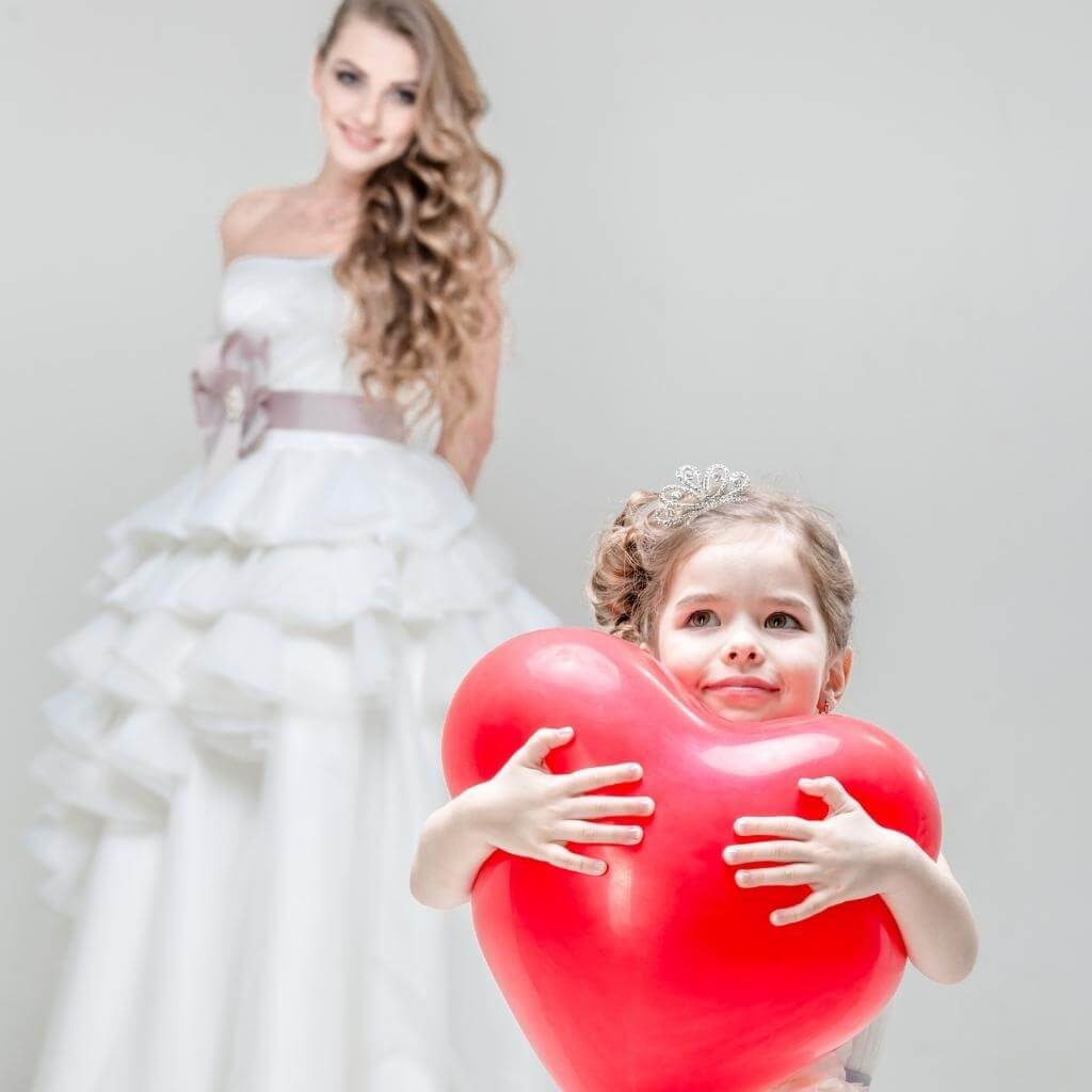 Hochzeitsfoto Idee mit Kind: Mädchen hält einen großen Herz Luftballon in der Hand und die Braut steht im Hintergrund