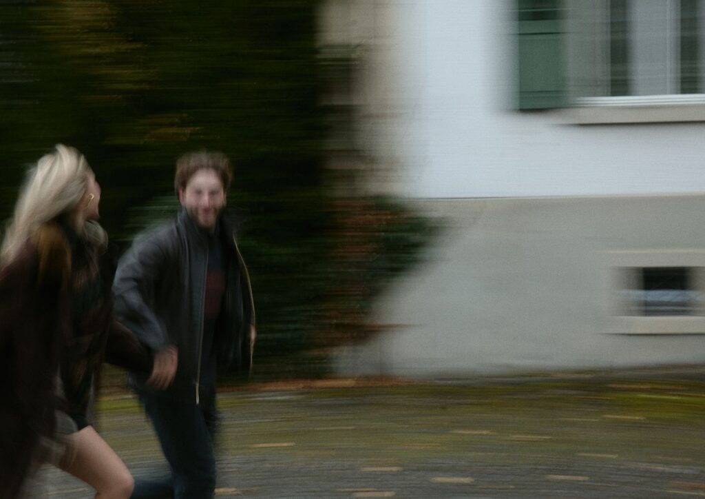 Verlobtes Paar läuft lachend durch eine urbane Umgebung mit Bewegungsunschärfe