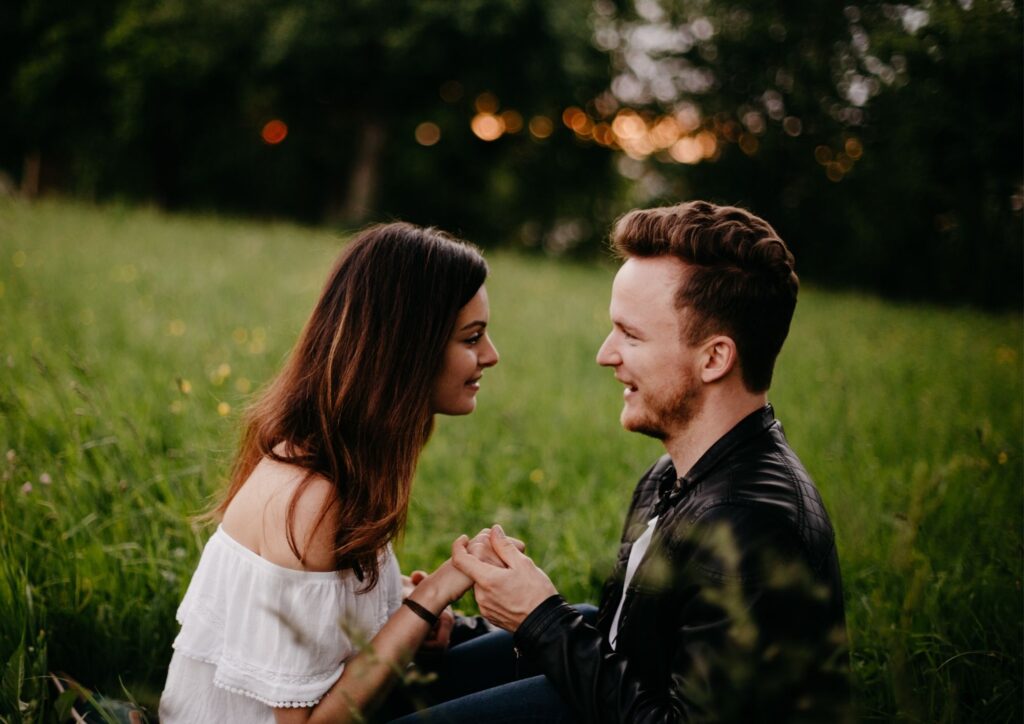 Paar sitzt auf einer Wiese und schaut sich verliebt an