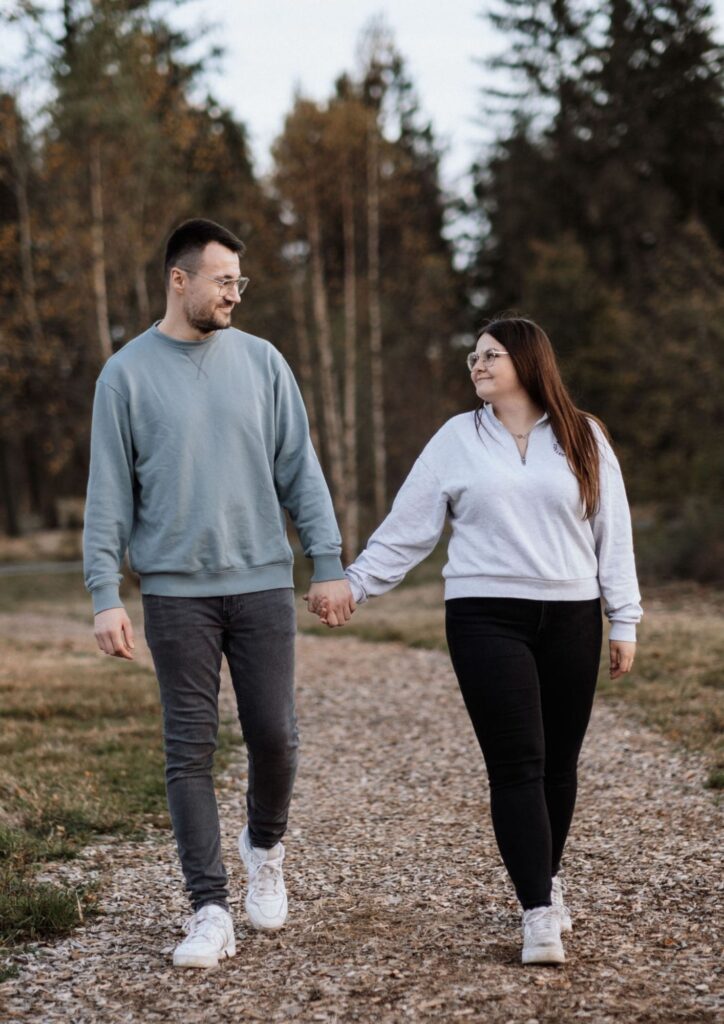 Verlobtes Paar geht Hand in Hand einen Waldweg entlang